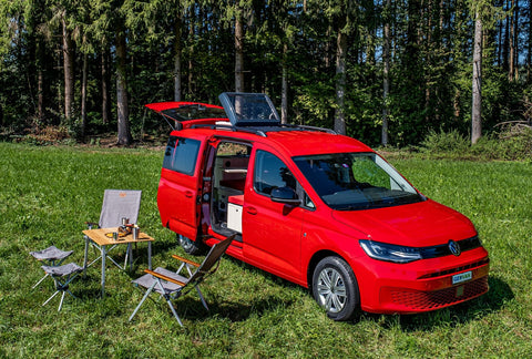 Roter VW-Minicamper mit Aufstelldach und Campingmöbeln auf einer Wiese